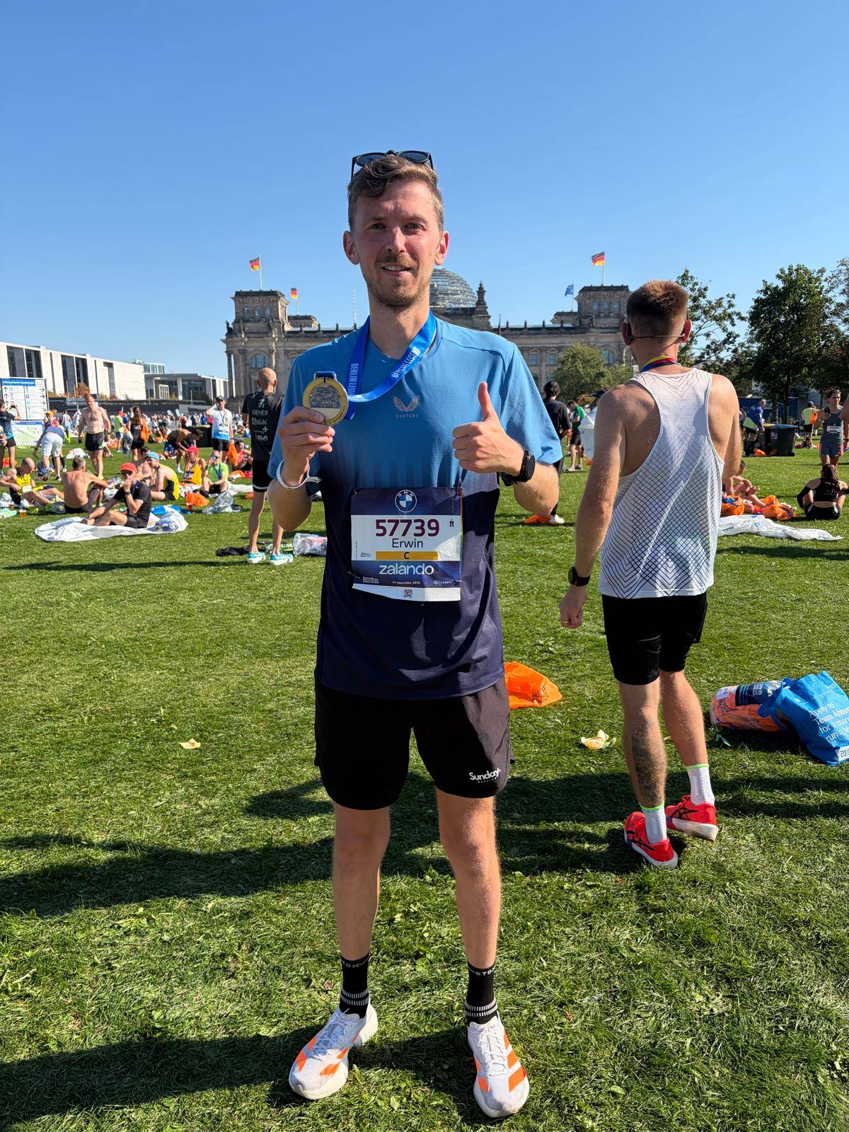 Erwin na de finish van de Marathon van Berlijn, met zijn medaille en een duim omhoog, voor de Rijksdag.
